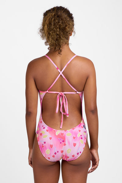 Female model wearing the Women’s Jackson One Piece Swimsuit in the Berry Zest print, standing in front of a grey background, shown from back view. 