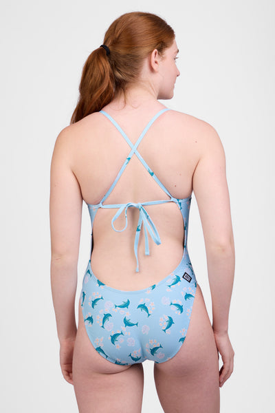 Female model wearing the Women’s Jackson One Piece Swimsuit in the Dolphrenz print, standing in front of a grey background, shown from back view. 