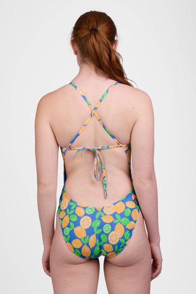 Female model wearing the Women’s Jackson One Piece Swimsuit in the Lemon Lime print, standing in front of a grey background, shown from back view. 