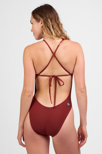 Female model wearing the Women’s Jackson One Piece in the Paprika solid, standing in front of a grey background, shown from back view. 
