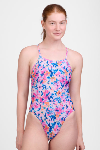 Female model wearing the Women's Julian Swim One Piece in the Superbloom print, standing in front of a grey background, shown from front view. 
