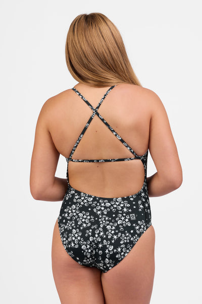 Female model wearing the Women's Marie One Piece Swimsuit in the Shells print, standing in front of a grey background shown from the back view