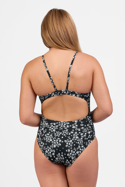 Female model wearing the Women's Tabitha One Piece Swimsuit in the Shells print, standing in front of a grey background shown from the back view