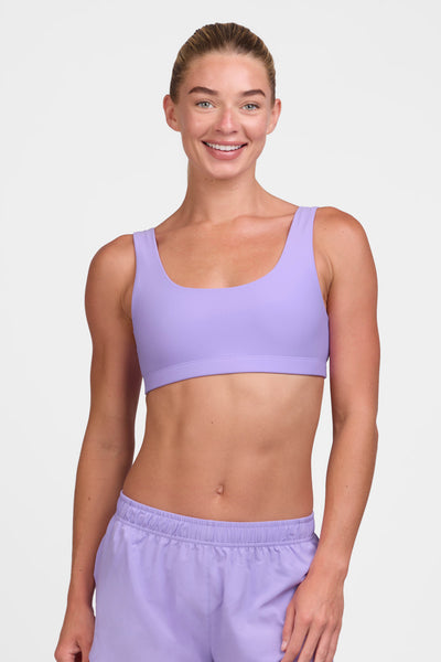 Female model wearing the Women's Arabella Sports Bra in the Lilac Haze solid, standing in front of a grey background shown from the front view 

|| Size S, Bust 33"