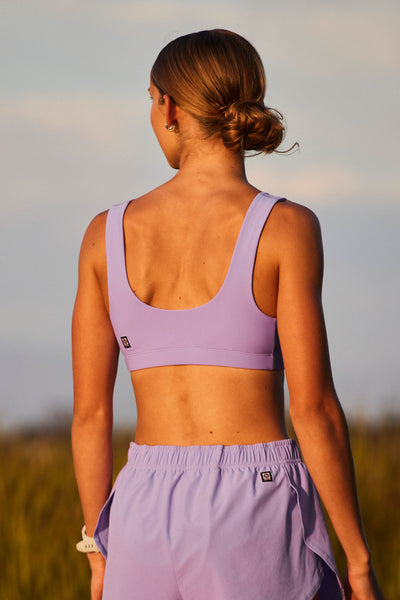 Female model wearing the Women's Arabella Sports Bra in the Lilac Haze solid, standing in front of a green and white background shown from the side view 

|| Size S, Bust 32"