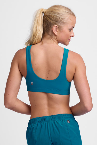 Female model wearing the Women's Arabella Sports Bra in the Space solid, standing in front of a grey background, shown from the back view.