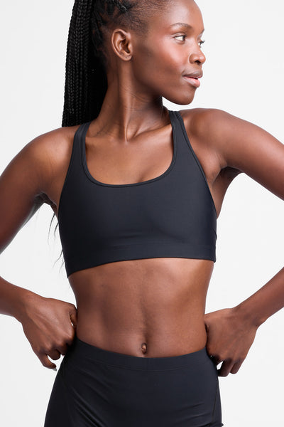 Female model wearing the Women's Molly Sports Bra in the Black solid, standing in front of a grey background, shown from the front view.