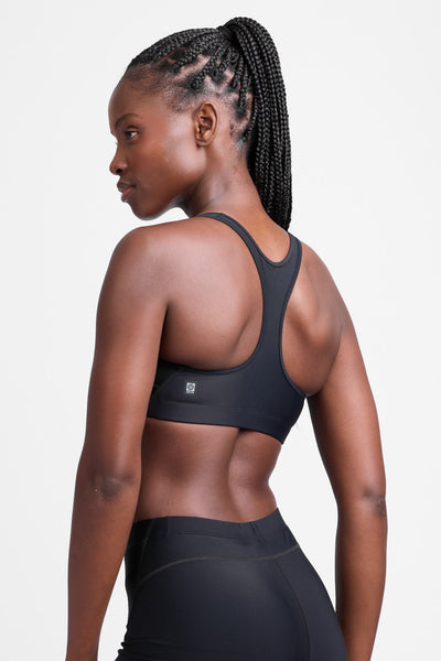 Female model wearing the Women's Molly Sports Bra in the Black solid, standing in front of a grey background, shown from the side view.