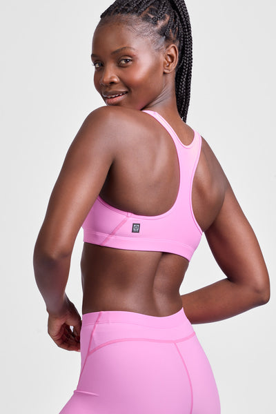 Female model wearing the Women's Molly Sports Bra in the Pinky solid, standing in front of a grey background, shown from the side view.