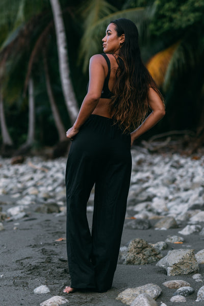 Female model wearing the Women's Alani Pants in the Black solid, standing in front of a beach shown from the back view

|| Size S, Height 5'4"  