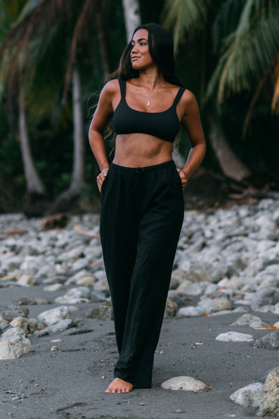 Female model wearing the Women's Alani Pants in the Black solid, standing in front of a beach shown from the front view

|| Size S, Height 5'4"  