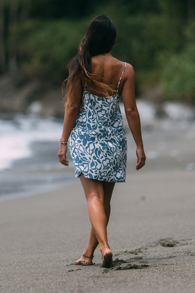 Female model wearing the Women's Nina Dress in the Pua print, standing in front of a beach shown from the back view

|| Size S, Height 5'4"  