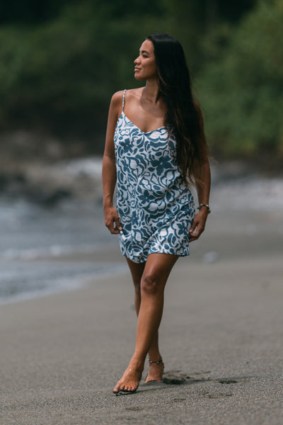 Female model wearing the Women's Nina Dress in the Pua print, standing in front of a beach shown from the front view

|| Size S, Height 5'4"  